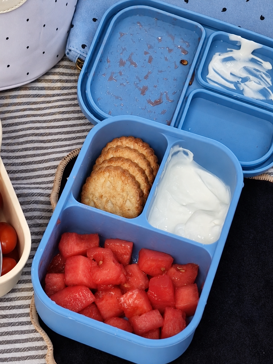 Enfant assis sur un plaid qui mange un sandwich, lunch box ouverte devant lui