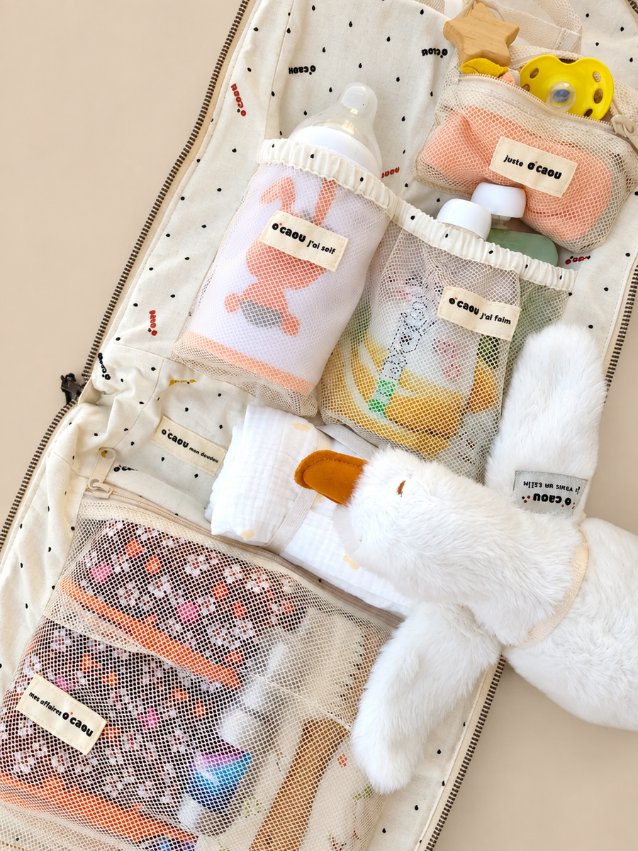 Sac ouvert : biberon, lingettes, couches et doudou rangés dans les poches étiquetées