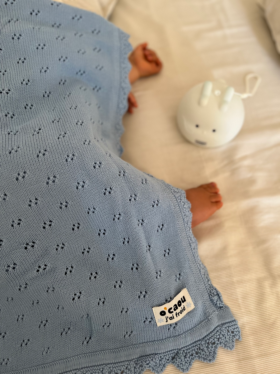 Couverture ajourée bleue étendue près d'un bébé, veilleuse posée à côté