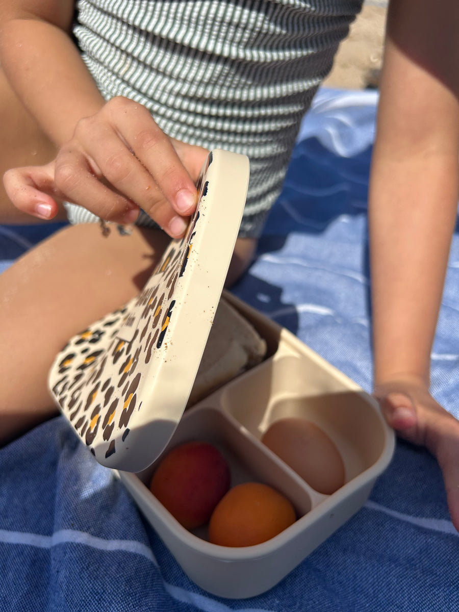 Lunch box ouverte pendant un pique-nique, couvercle léopard tenu à la main