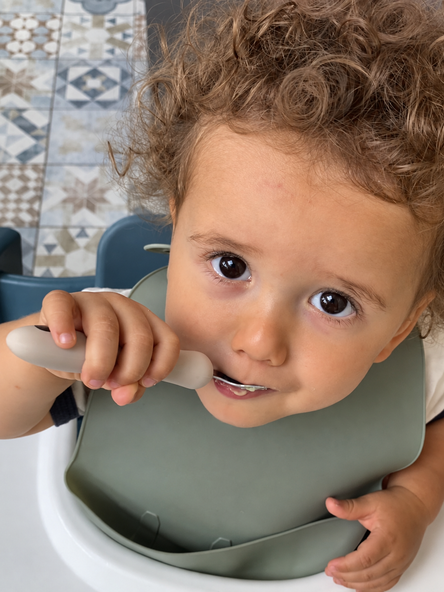 Enfant dans sa chaise haute qui mange seul avec sa cuillère