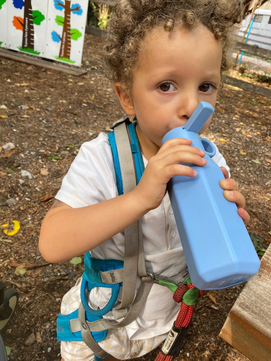 Enfant qui boit à sa gourde bleue, sac à dos sur les épaules