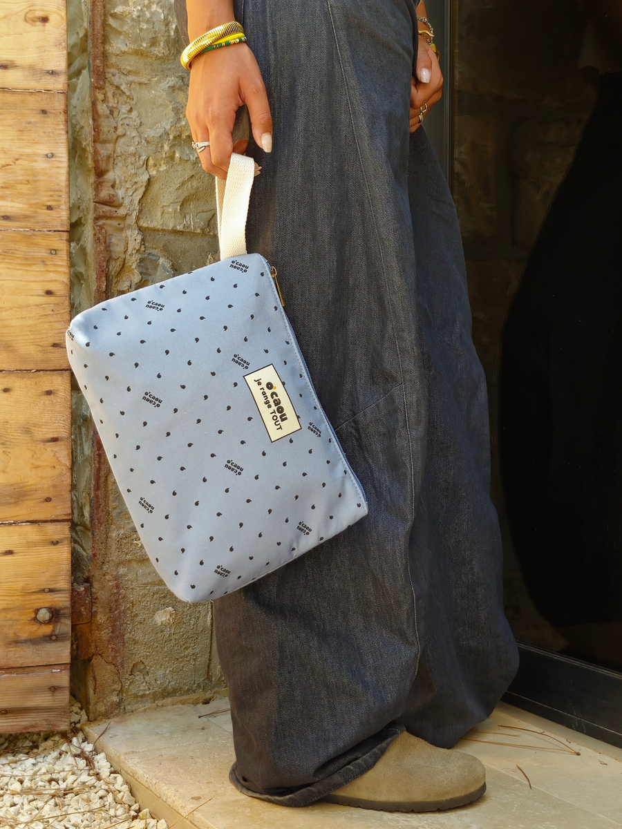 Pochette bleue tenue par sa poignée, devant une porte