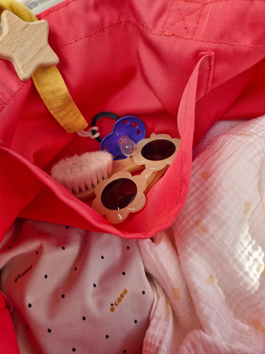 Intérieur d'un cabas rose : poche zippée, lunettes de soleil et petits jouets