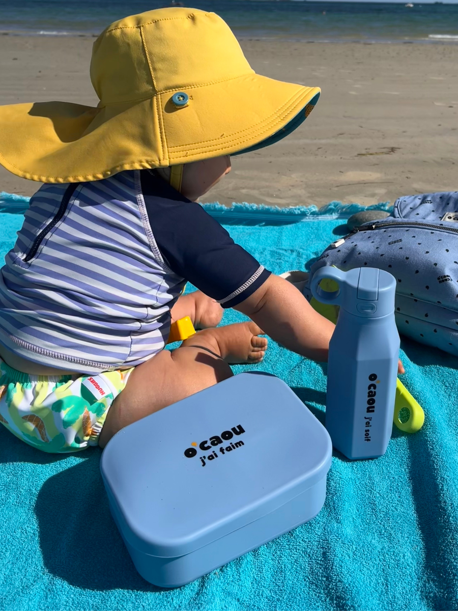 Sac isotherme ouvert sur l'herbe, lunch box rose et couverts à l'intérieur
