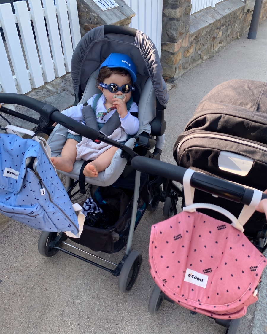 Deux sacs O'CAOU accrochés aux guidons de poussettes, un enfant installé dans l'une d'elles