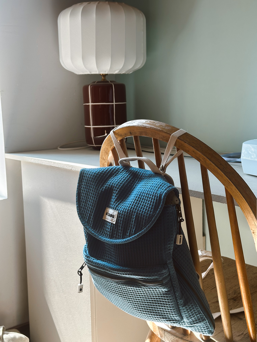 Sac O'CAOU bleu posé sur le dossier d'une chaise en bois, dans une chambre