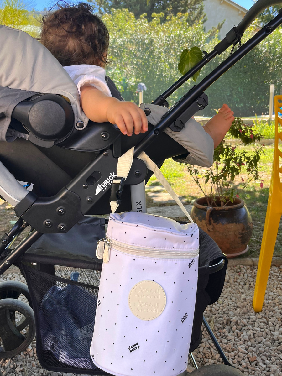 Sac isotherme rose accroché à la poussette, dans un jardin