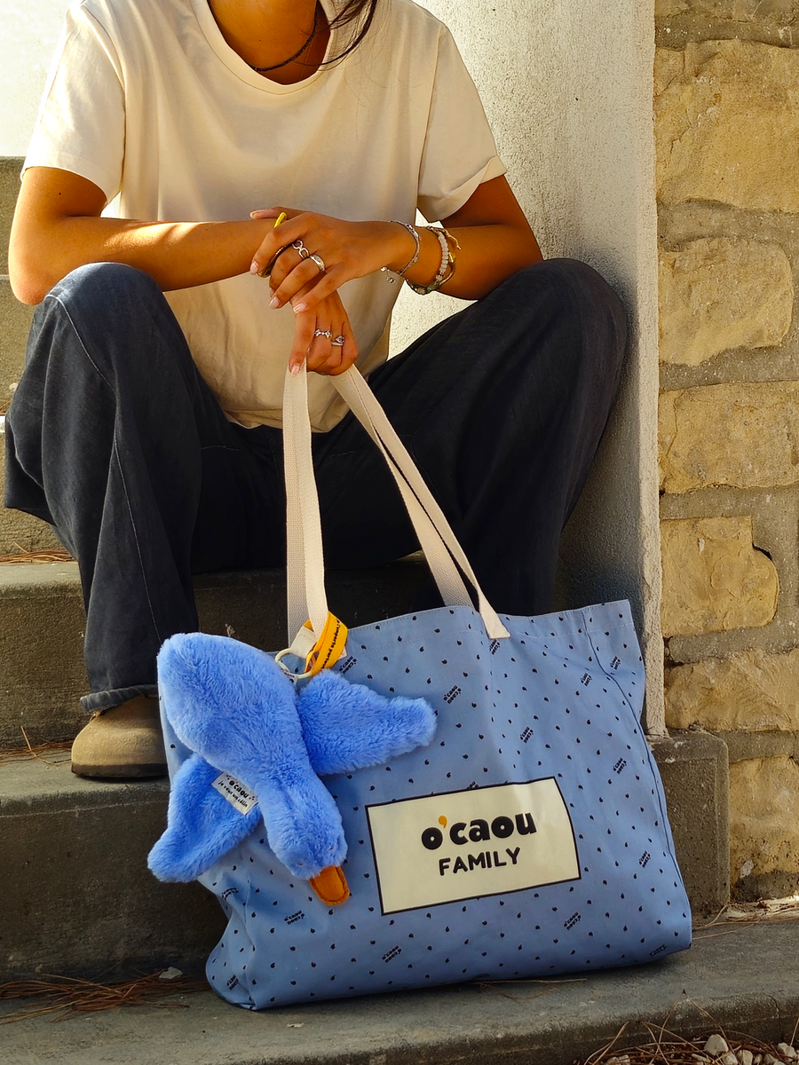 Cabas bleu porté à l'épaule, doudou accroché à l'anse