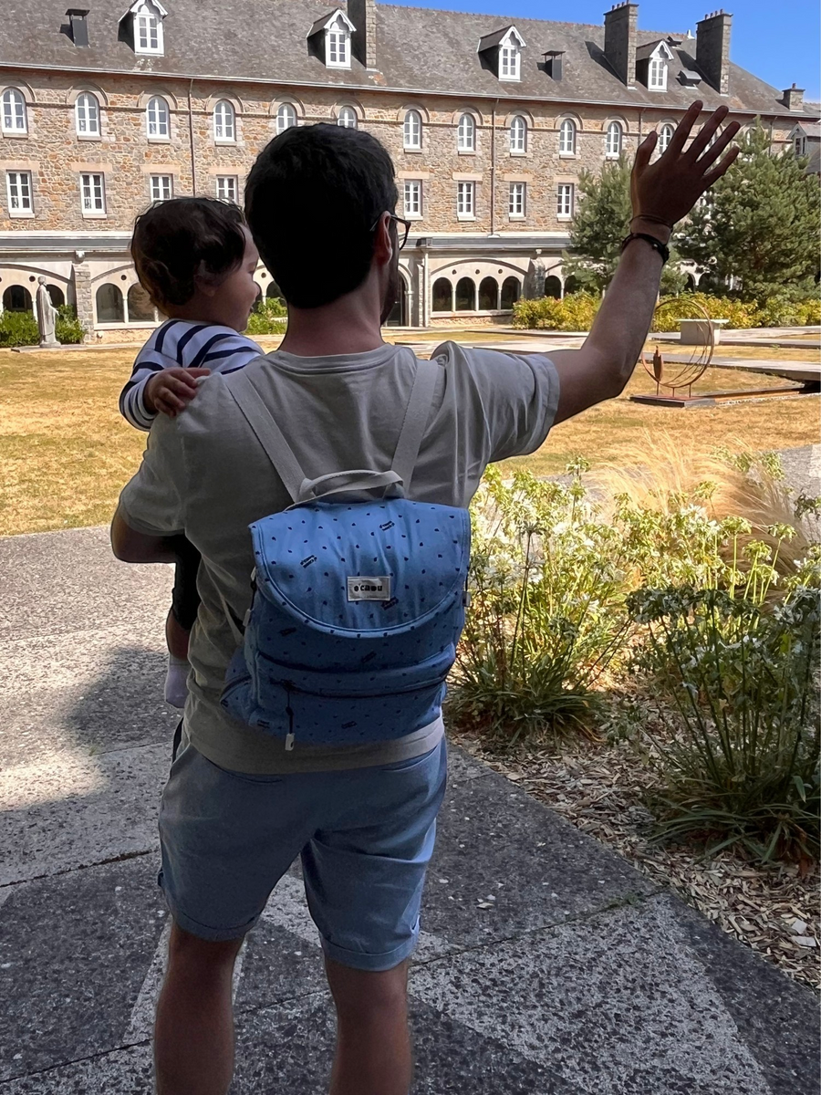 Adulte de dos portant un enfant dans les bras et le sac à dos bleu