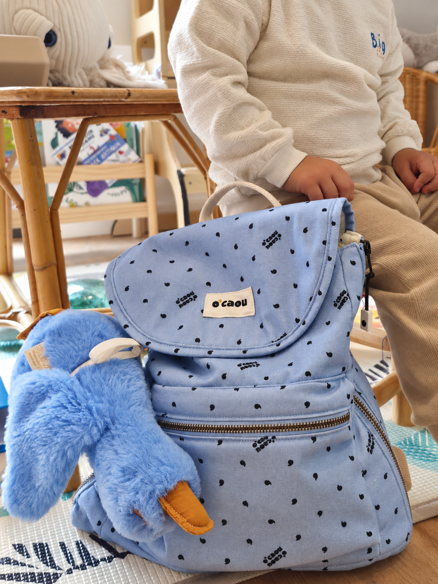 Sac à dos bleu posé sur un plaid, doudou accroché à l'extérieur